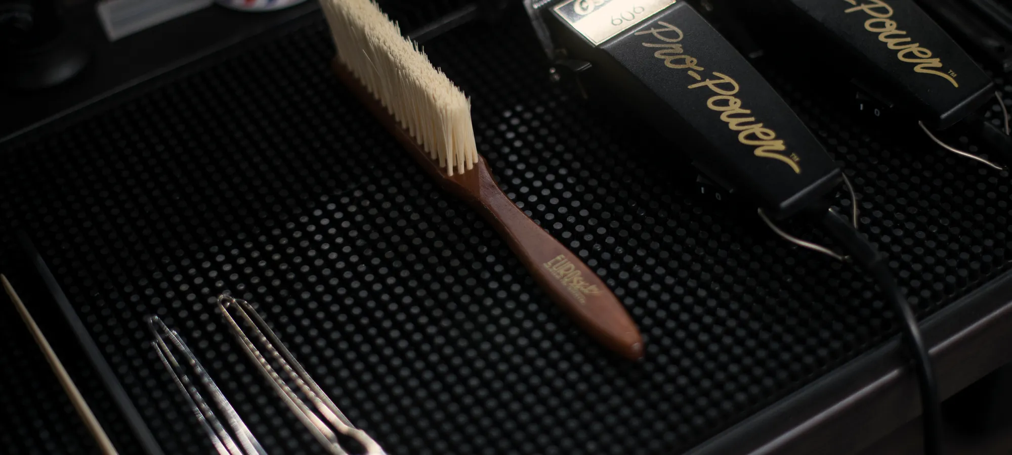 Tondeuses, ciseaux et brosse de barbier posés sur un plateau noir